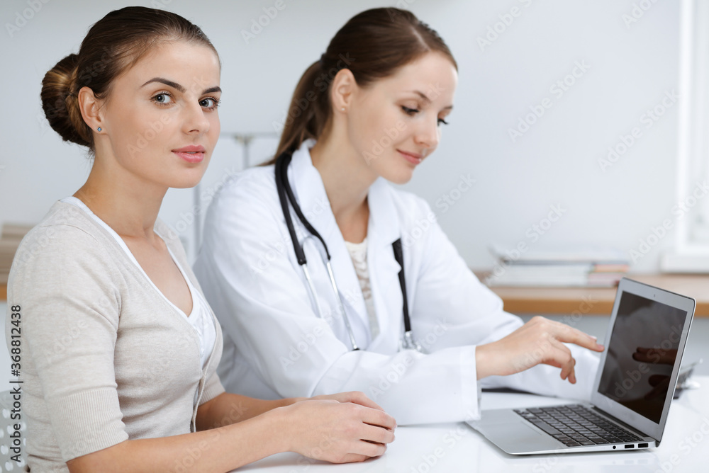 Doctor and patient are sitting and discussing health examination results while using laptop computer. Health care, medicine and good news concepts