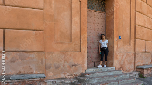 Woman in har, black pants, tshirt and sneakers holding phone in doorway