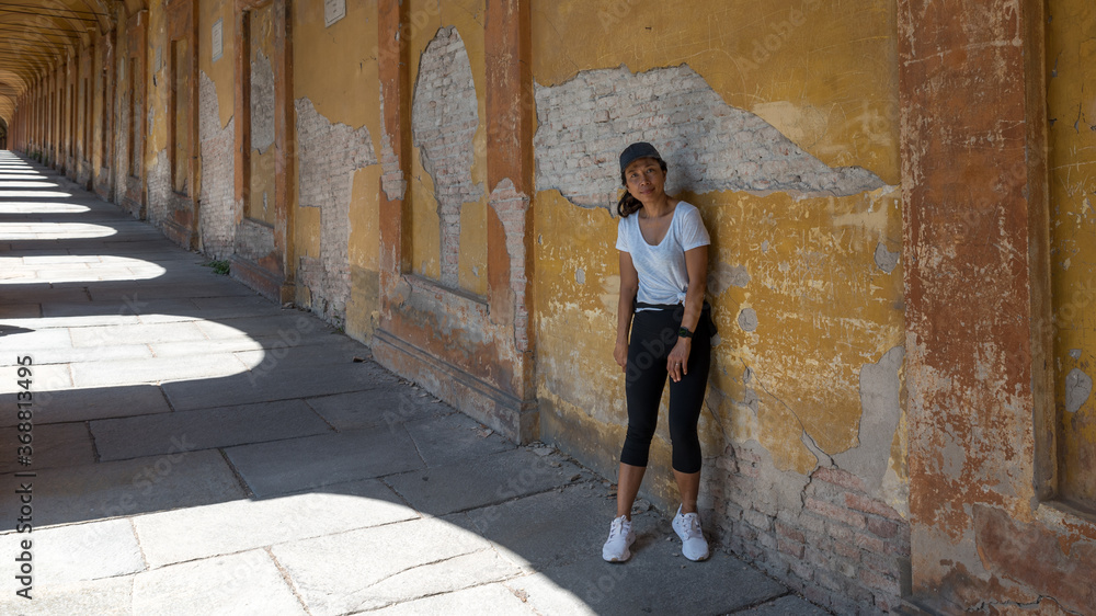 Woman in had and sneakers leaning against an old wall in a portico
