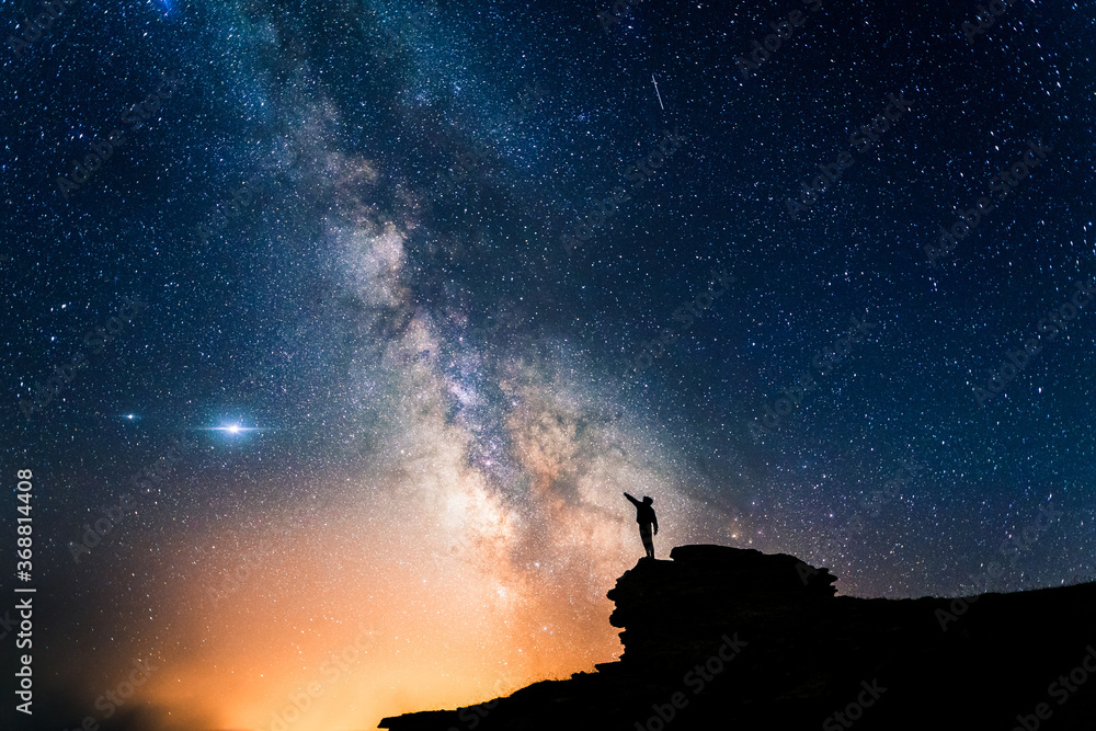 Person pointing the Milky Way with his hand. Small human silhouette contemplating the immensity of the universe under a magical starry sky. Concept of human smallness.