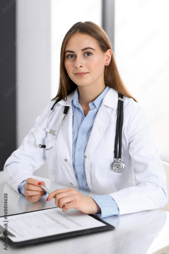 Doctor woman filling up medical form while sitting at the desk in hospital office. Physician at work. Medicine and health care concept Doctor woman filling up medical form while sitting at the desk in hospital office. Physician at work. Medicine and health care concept