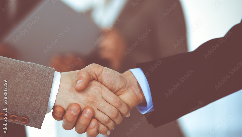 Business people shaking hands while standing with colleagues after meeting or negotiation, close-up. Group of unknown businessmen and women in modern office. Teamwork, partnership and handshake Business people shaking hands while standing with colleagues after meeting or negotiation, close-up. Group of unknown businessmen and women in modern office. Teamwork, partnership and handshake