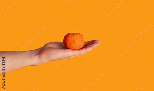 Millennial man showing tangerine fruit over orange background, closeup of hand. Copy space