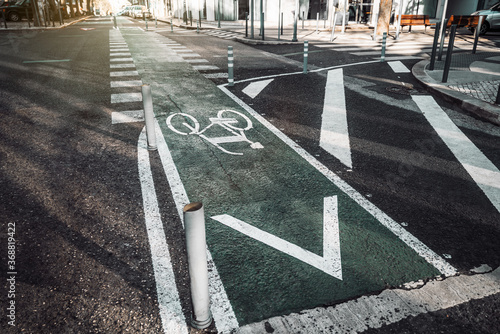 Wide-angle view of a modern urban crossroad with marking and bicycle sign on asphalt, and a pedestrian crossing in a distance, plastic posts in the foreground, Lisbon, Arroios district, Portugal
