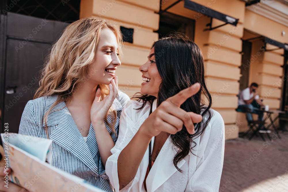 European girls exploring city with map. Laughing blonde lady travelling with friend. European girls exploring city with map. Laughing blonde lady travelling with friend.