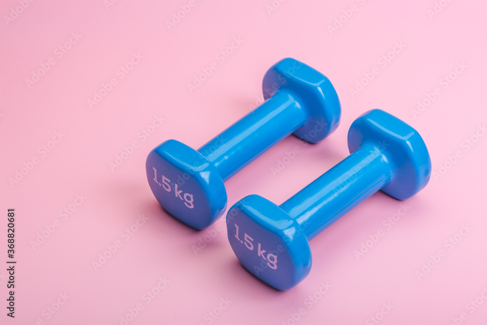 A pair of blue dumbbells on a pink background A pair of blue dumbbells on a pink background