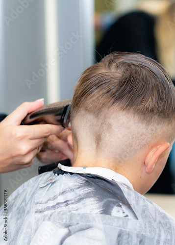 Vertical image Back view Close up caucasian pretty school boy trendy haircut at bright modern barbershop.