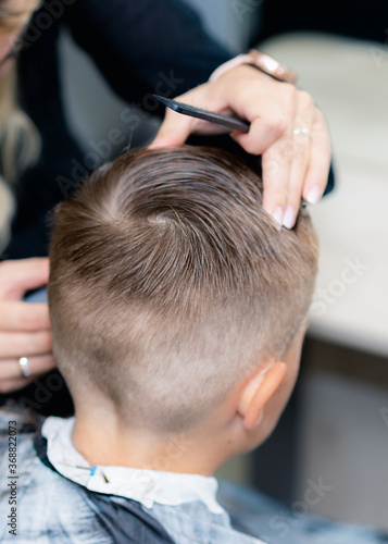 Close up caucasian american pretty school boy trendy haircut at bright modern barbershop.