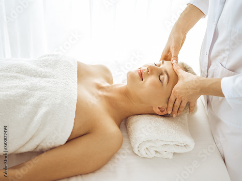 Beautiful blonde woman enjoying facial massage with closed eyes. Relaxing treatment in medicine and spa center concepts