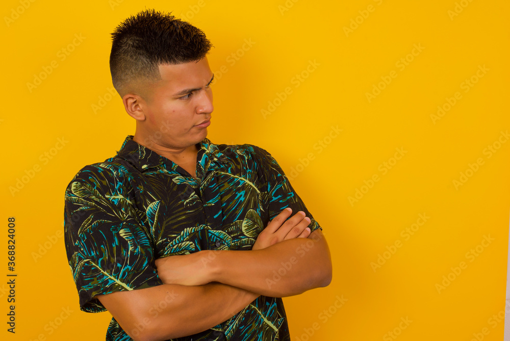 Image of upset pretty young caucasian man standing indoors with arms crossed. Looking with disappointed expression aside after listening to bad news. Confident young man. Image of upset pretty young caucasian man standing indoors with arms crossed. Looking with disappointed expression aside after listening to bad news. Confident young man.