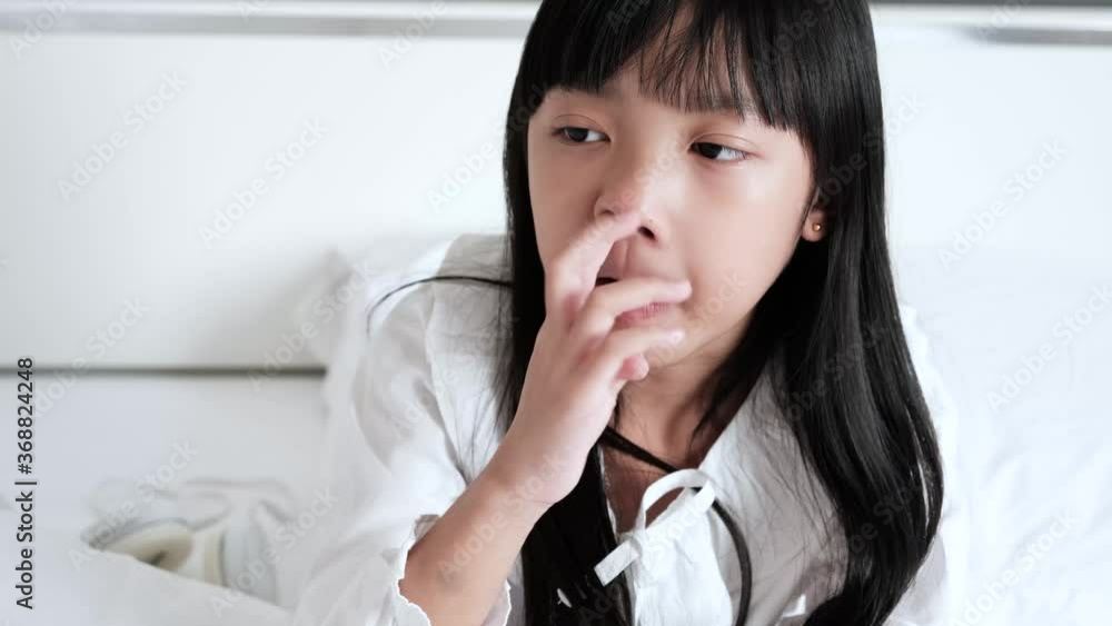 Asian child girl in a white dress is picking her nose on the bed. Asian child girl in a white dress is picking her nose on the bed.