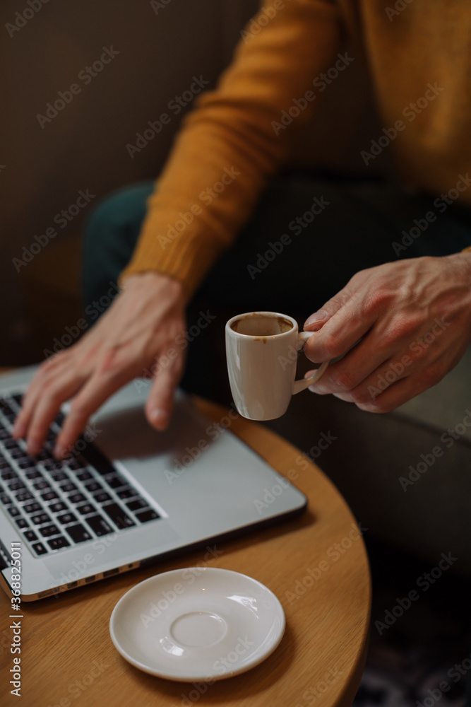 Cropped unrecognizable man drinking espresso and working on laptop in coffee shop. Cropped unrecognizable man drinking espresso and working on laptop in coffee shop.