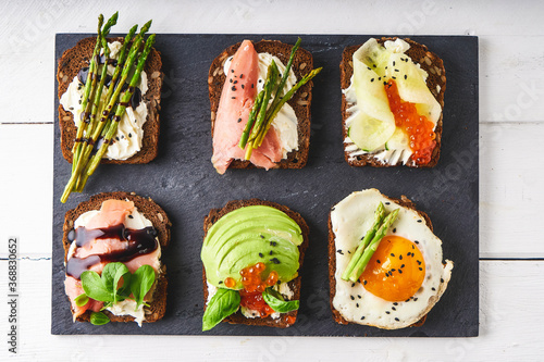 several healthy sandwiches with different fillings. Fish, caviar, avocado, asparagus, cucumber, herbs, sesame seeds, gluten-free bread served on a dark platter