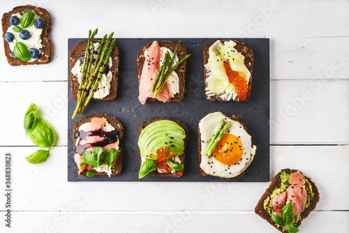 several healthy sandwiches with different fillings. Fish, caviar, avocado, asparagus, cucumber, herbs, sesame seeds, gluten-free bread served on a dark platter