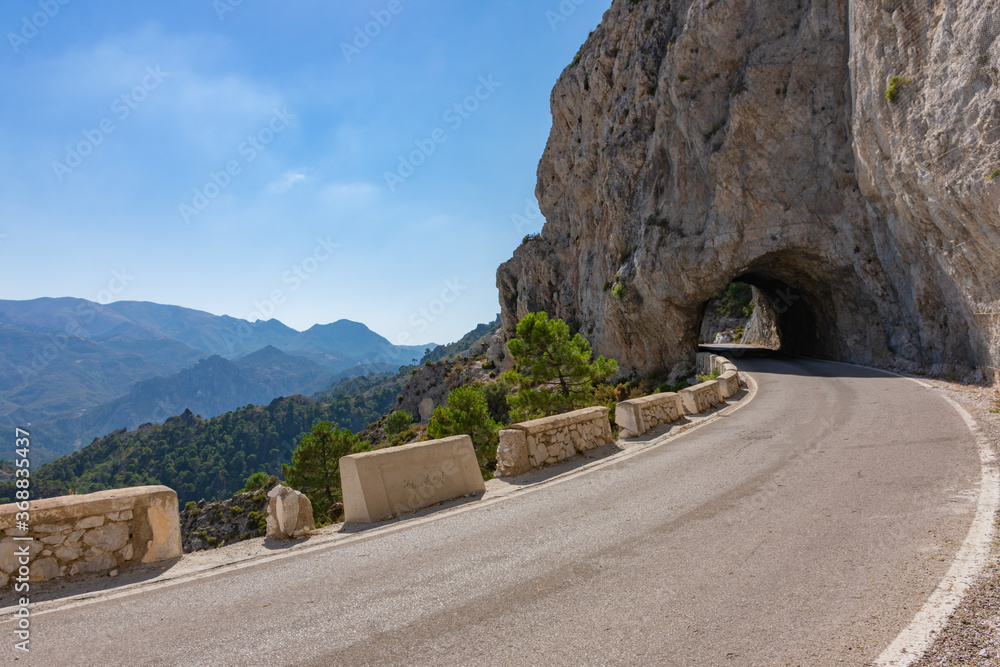 Narrow high mountain road with a tunnel made of stone and views of other peaks, is known as Carretera de la Cabra, Granada, Spain.
