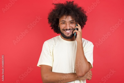 Portrait of a smiling young casual successful man talking on mobile phone isolated over yellow background. Business, confidence and communication concept.