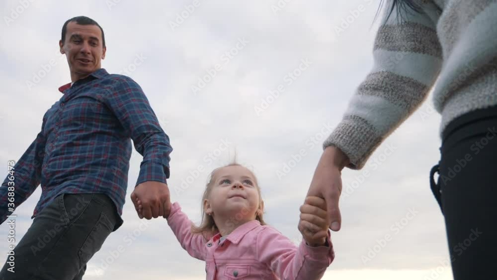 A happy family walks in the Park under the rays of the sun at sunset. Mom, dad and baby holding hands walk in the fresh air, lead a healthy lifestyle.