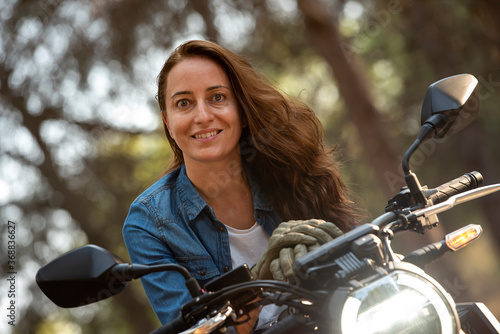 A cheerful young woman with loose, brown hair on a big bike. © Chebix