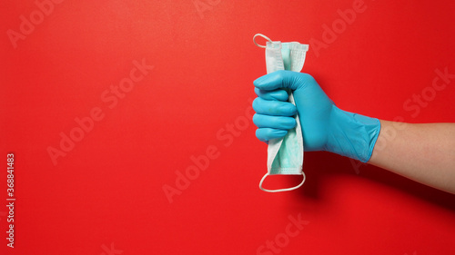 Hand wear glove and holding face Mask on red background.