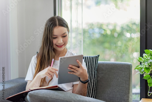 Beautiful young asian woman working on tablet while sitting at the living room at home.