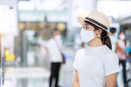Young adult female wearing face mask in airport terminal, protection Coronavirus disease infection, Asian woman traveler with hat ready to travel. New Normal and travel under COVID-19 concept © Jo Panuwat D