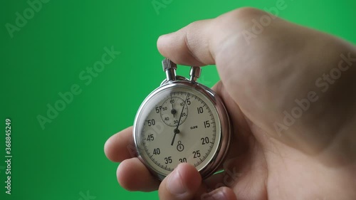 Male hand holding analogue stopwatch on green screen chroma key. Time start with old chronometer man presses start button in the sport concept. Time management concept. photo