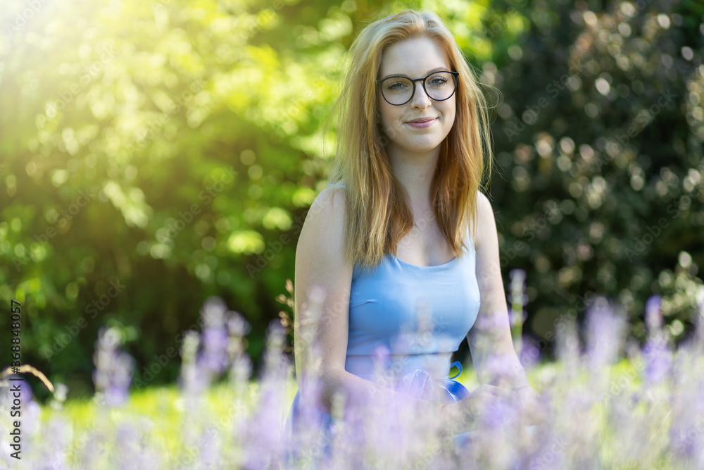 Smiling young woman is posing with glasses behind lavender in the garden Smiling young woman is posing with glasses behind lavender in the garden