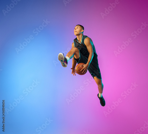 Winner. Young basketball player in action, motion in high jump on gradient background in neon. Concept of sport, movement, energy and dynamic, healthy lifestyle. Training, practicing, trendy colors.