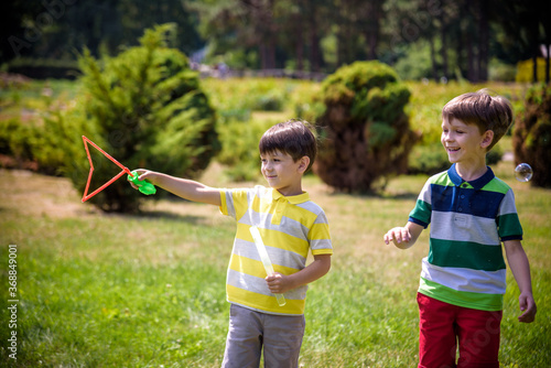 Boy blowing soap bubbles while an excited kid enjoys the bubbles. Happy teenage boy and his brother in a park enjoying making soap bubbles. Happy childhood friendship concept