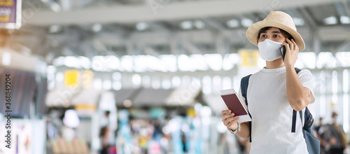 Young adult female with face mask holding passport and smartphone in airport, protection Coronavirus disease infection, Asian woman traveler check flight. New Normal and travel under COVID-19 concept