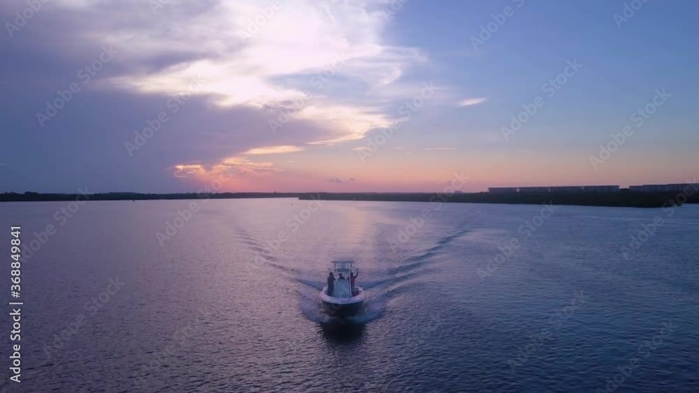 DRONE BACKWARDS AS BOAT DRIVES TOWARDS AT SUNSET DRONE BACKWARDS AS BOAT DRIVES TOWARDS AT SUNSET