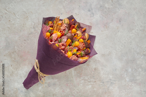 Tasty edible bouquet consisting of sausages, cheese and tomatoes on a light background.