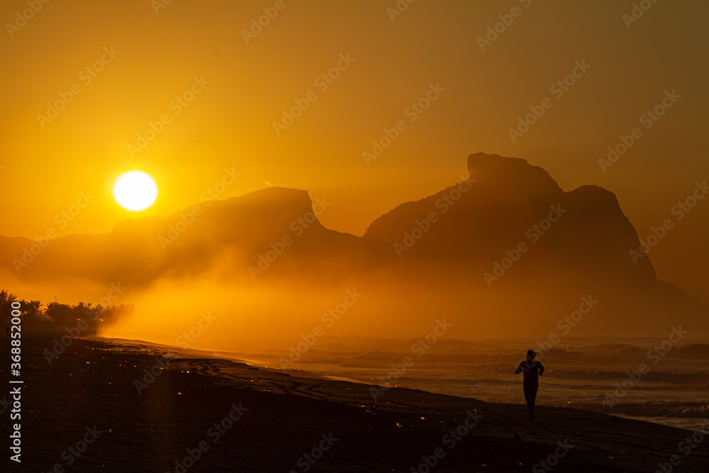 silhueta de um homem exercitando-se na praia ao nascer do sol, com a bela pedra da Gávea em segundo plano silhueta de um homem exercitando-se na praia ao nascer do sol, com a bela pedra da Gávea em segundo plano