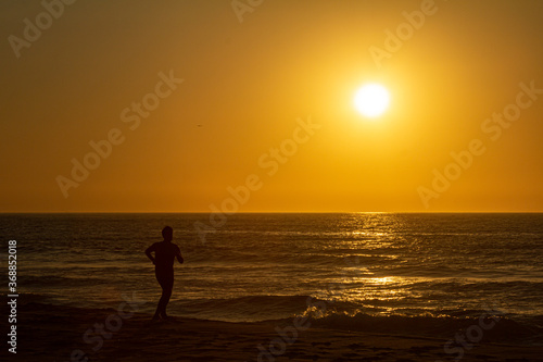 silhueta de um homem correndo à beira do mar ao nascer do sol