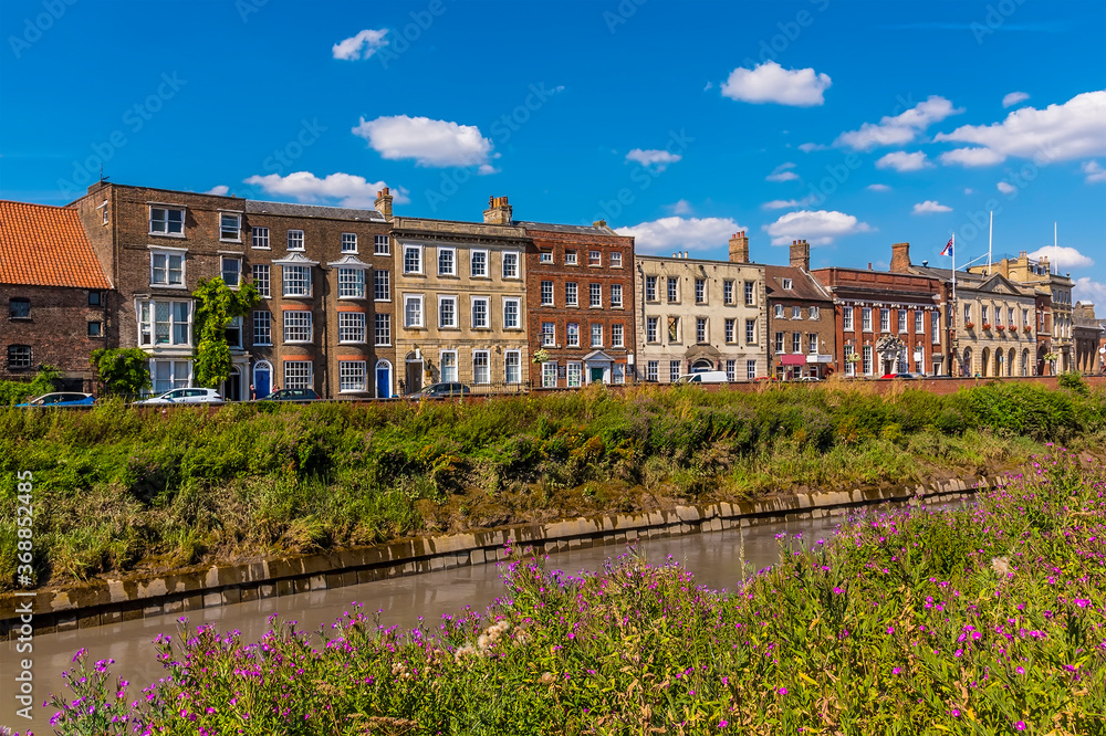 Fototapeta premium A view along the River Nene towards Georgian buildings on the North Brink in Wisbech, Cambridgeshire in the summertime