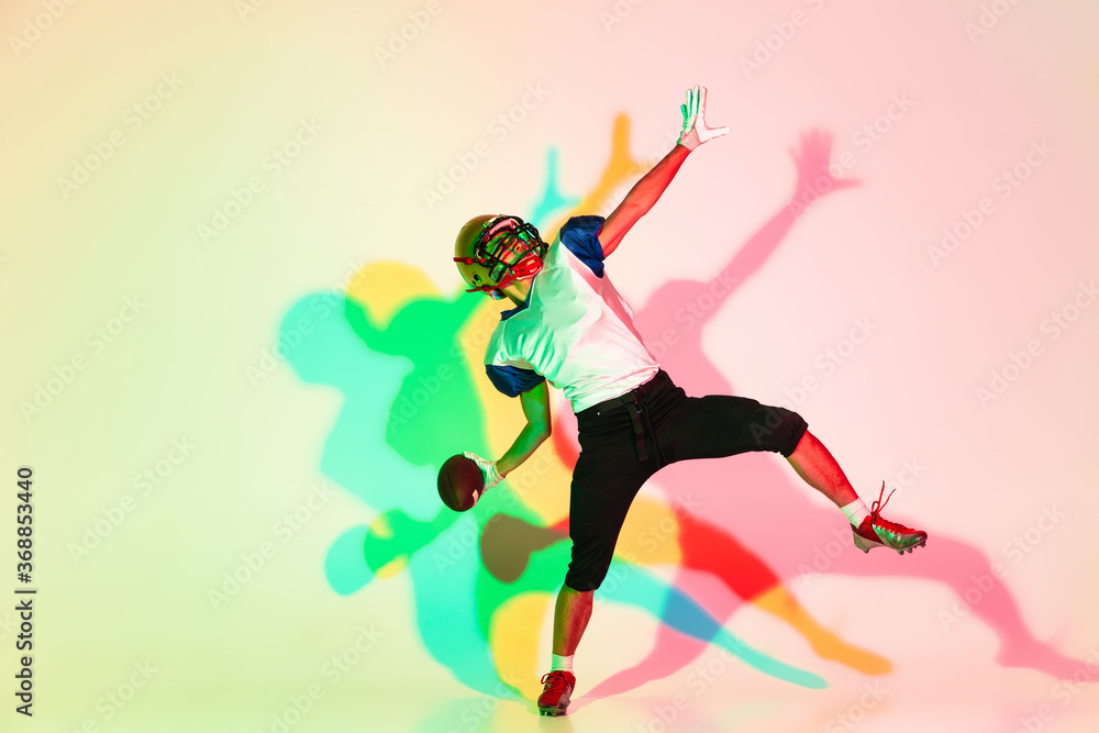 American football player isolated on gradient studio background in neon light with shadows. Professional sportsman during game playing in action and motion. Concept of sport, movement, achievements. American football player isolated on gradient studio background in neon light with shadows. Professional sportsman during game playing in action and motion. Concept of sport, movement, achievements.
