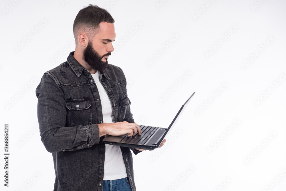 A man in jeans. A bearded man is holding a laptop. A person is typing on a laptop. A man stands sideways to the camera on a white background. A man in jeans. A bearded man is holding a laptop. A person is typing on a laptop. A man stands sideways to the camera on a white background.