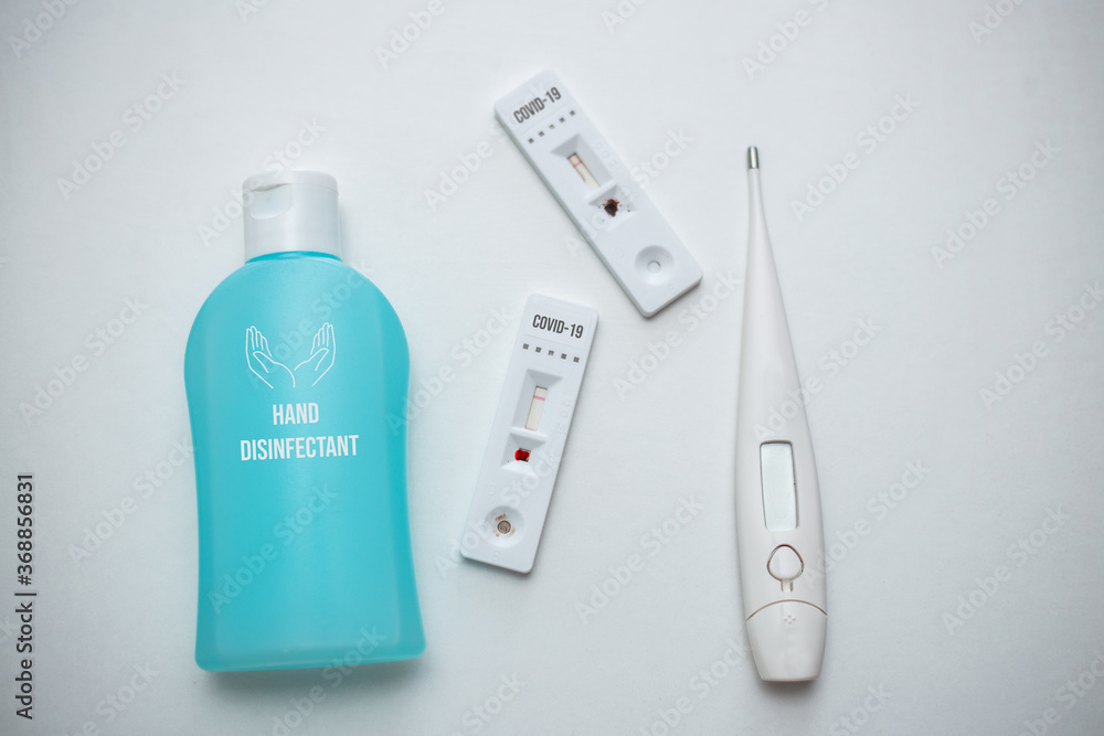 Two covid-19 rapid tests, hand desinfectant and a thermometer on white table isolated Two covid-19 rapid tests, hand desinfectant and a thermometer on white table isolated