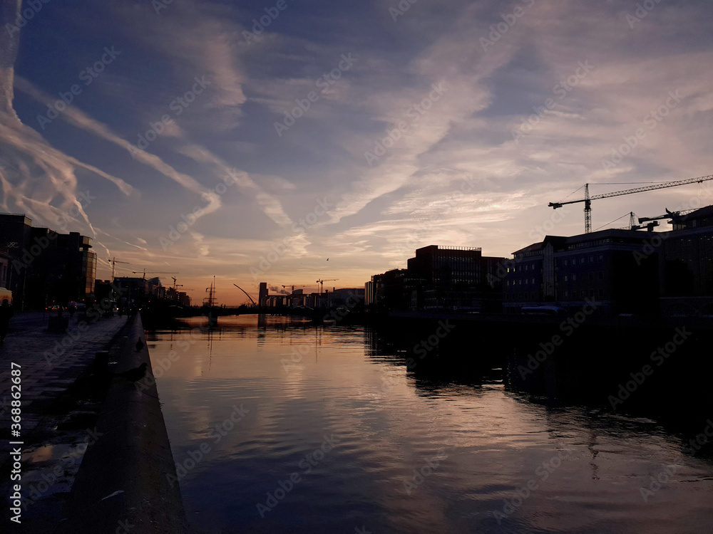 Sunrise over the River Liffey in Dublin, with the port on the horizon and silhouettes of the buildings on the sides.