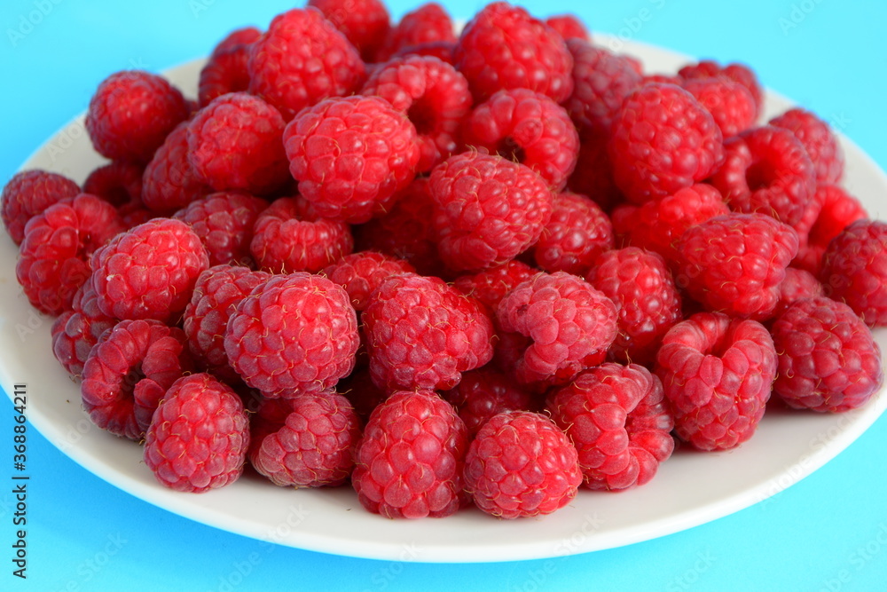 Fresh raspberry on plate close up isolated on light blue background,close up. Summer berries. Fresh raspberry on plate close up isolated on light blue background,close up. Summer berries.