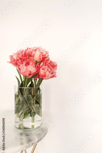Beautiful pink peony flowers bouquet in glass vase on marble table on white background