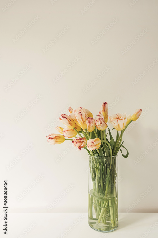 Yellow tulip flowers bouquet in glass vase against the white wall. Holiday celebration concept. Interior decoration.