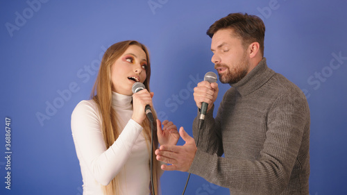 Young caucasian couple singing karaoke. Isolated on the blue background. High quality photo