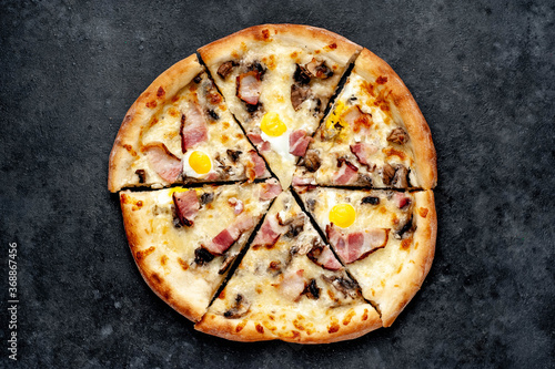 Pizza carbonara with bacon, cheese, mushrooms, quail eggs, creamy sauce on a stone background