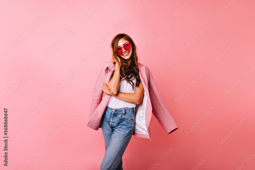 Spectacular ginger girl in denim pants having fun while posing in studio. Fashionable white young lady in jacket smiling to camera. Spectacular ginger girl in denim pants having fun while posing in studio. Fashionable white young lady in jacket smiling to camera.
