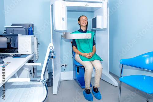 A happy teenage girl is sitting in an x-ray machine at a dentist s clinic