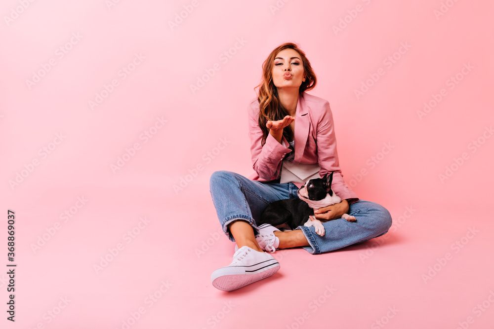 Romantic girl in stylish outfit sending air kiss during photoshoot with her dog. Indoor portrait of blithesome ginger woman having fun with pet. Romantic girl in stylish outfit sending air kiss during photoshoot with her dog. Indoor portrait of blithesome ginger woman having fun with pet.