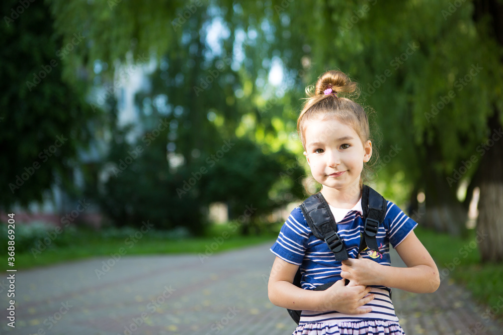 A little girl of Caucasian appearance in a school uniform with a backpack looks into the frame. Concept back to school. Elementary school, developing activities for preschoolers. Space for text A little girl of Caucasian appearance in a school uniform with a backpack looks into the frame. Concept back to school. Elementary school, developing activities for preschoolers. Space for text