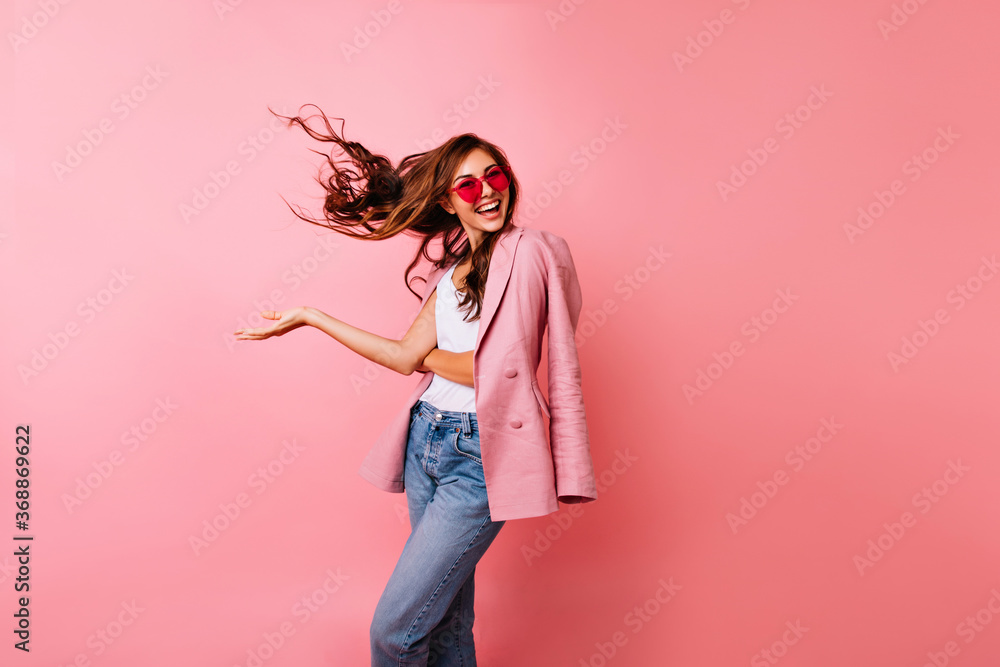 Excited good-looking girl in sunglasses dancing in studio. Ginger blissful woman posing on rosy background with hair waving. Excited good-looking girl in sunglasses dancing in studio. Ginger blissful woman posing on rosy background with hair waving.
