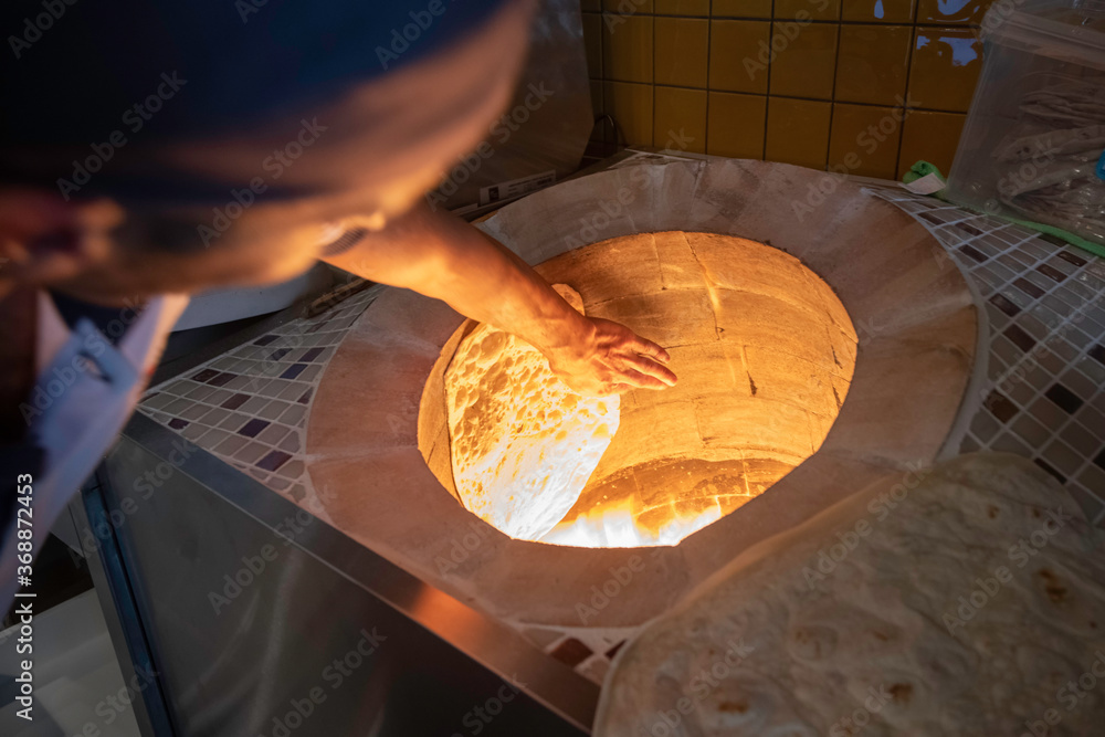chef in a kitchen placing pita bread while the traditional Turkish oven in  burning Stock Photo